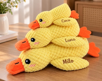 Peut inclure: Trois canards en peluche jaunes avec des becs et des pattes orange, fabriqués dans un tissu texturé en nid d'abeille. Chaque canard a des yeux noirs brodés, des joues roses et un prénom cousu sur l'aile : Coco, Luna et Milo.