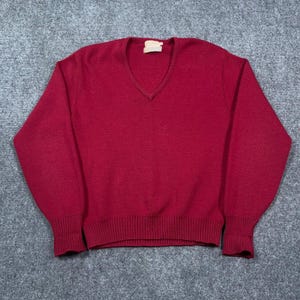 Pode incluir: Uma camisola de manga comprida em vermelho escuro sólido com decote em V e punhos e bainha canelados. A peça apresenta uma textura de malha simples em toda a superfície e inclui uma pequena etiqueta de marca retangular clara no interior.
