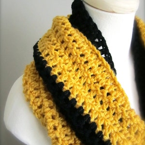 May include: A yellow crocheted infinity scarf with a black crocheted trim. The scarf is displayed on a white mannequin.