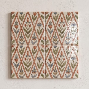 May include: Four square ceramic tiles arranged in a grid, featuring a repeating diamond lattice pattern in terracotta orange. Inside each diamond, stylized floral motifs in muted blue, green, and orange tones are painted on a cream background.
