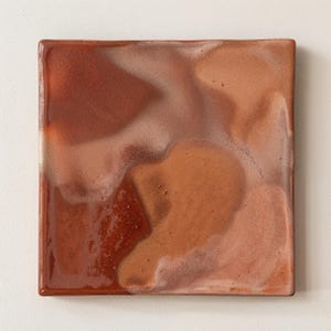 Op de afbeelding: Een vierkant keramieken bord met een glanzend, gemarmerd glazuur in tinten terracotta, roestoranje en zacht beige. Het oppervlak heeft een gladde, reflecterende afwerking met subtiele variaties in kleurdiepte en textuur over het vlak.