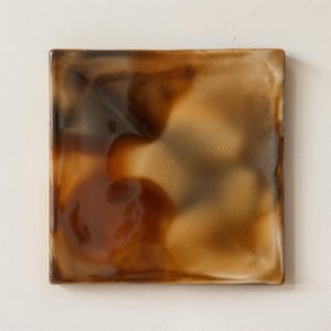 May include: A square ceramic plate with a glossy finish, featuring a blended colour palette of dark brown, caramel, and cream tones. The surface has a smooth, reflective texture with subtle variations in the glaze, creating a gradient effect.
