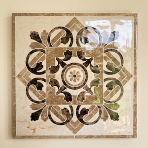 May include: A square ceramic tile featuring a glossy finish and a symmetrical pattern in shades of beige, cream, and dark brown. The design includes a central flower motif surrounded by intricate scrollwork, geometric lines, and marble-like textures.