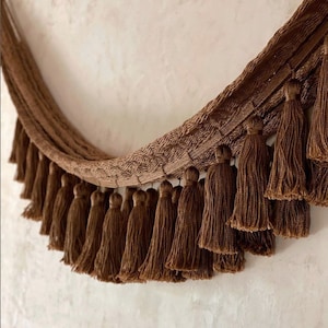 May include: A brown fabric curtain with a fringe of tassels. The tassels are made of the same fabric as the curtain and are arranged in a row.