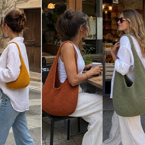 May include: A collection of three crochet hobo bags in mustard yellow, burnt orange, and olive green. Each bag features a crescent-shaped silhouette with a single integrated shoulder strap and a dense, textured knit pattern made from yarn.