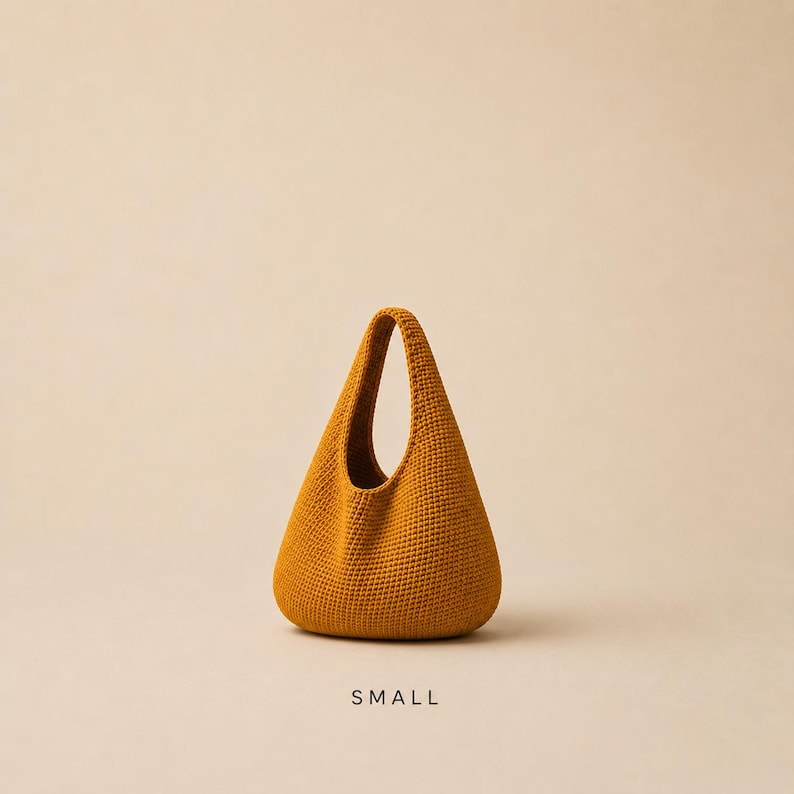 May include: A mustard yellow handbag with a teardrop-shaped silhouette and a single integrated handle. The bag features a dense, uniform knit texture throughout its exterior surface. The word SMALL is printed in black capital letters below the bag.