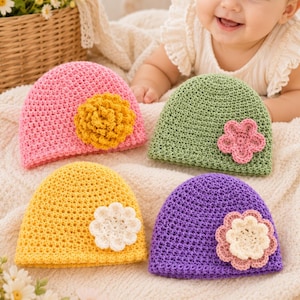 May include: Four crochet baby hats in pink, green, yellow, and purple. Each hat features a unique crocheted flower embellishment: a textured yellow flower on the pink hat, a pink five-petal flower on the green hat, a white flower on the yellow hat, and a layered pink and cream flower on the purple hat.
