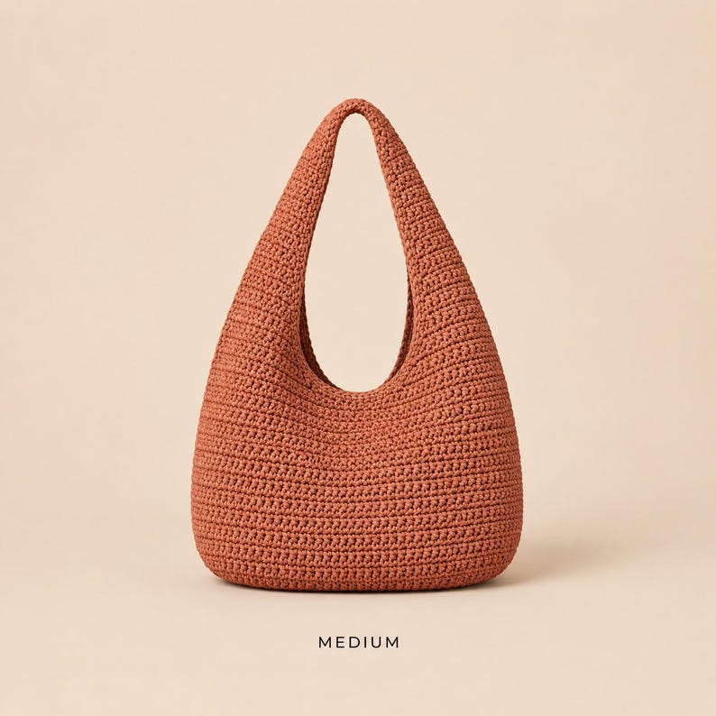 May include: A medium-sized, rust-coloured hobo bag crafted with a dense, textured crochet stitch. The bag features a single integrated shoulder strap that forms a continuous loop with the body, creating a rounded, teardrop-like silhouette.