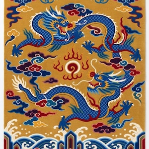 Op de afbeelding: Een rechthoekig vloerkleed met een mosterdgele achtergrond met twee blauwe draken die tegenover elkaar staan, rondom een centrale vlammende parel. Het ontwerp bevat gestileerde wolken, golven en diverse objecten aan de onderkant, afgewerkt met witte franje.