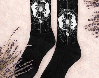 May include: A pair of black socks with a white design of two wolves howling at the moon with a constellation background. The text "Two Wolves" is written on the socks.