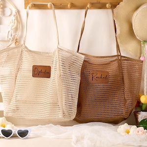 Puede incluir: Dos bolsos de malla con correas largas para el hombro, uno en color crema y otro en marrón. Cada bolso presenta un parche rectangular de aspecto de cuero marrón en el frente. El bolso crema tiene el nombre Ophelia y el marrón tiene Rachel.