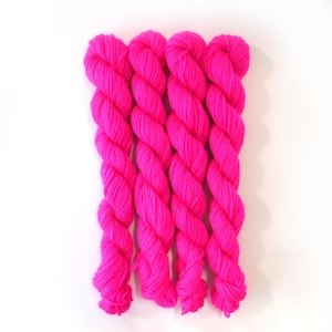 May include: Four skeins of vibrant pink yarn are arranged vertically against a white background. The yarn is tightly twisted, showcasing a rich, saturated color. This image is ideal for showcasing knitting or crochet supplies.