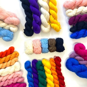 Peut inclure: Assortiment de pelotes de laine colorées dans différentes nuances de rose, bleu, vert, jaune, rouge, noir, blanc et violet. La laine est disposée en rangées et en colonnes sur une surface blanche.