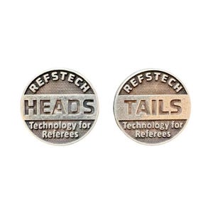 Könnte beinhalten: Zwei kreisförmige, silberfarbene Metallmünzen mit texturiertem Hintergrund. Eine Münze zeigt das Wort HEADS, die andere das Wort TAILS. Beide Münzen enthalten den Text REFSTECH und Technology for Referees in erhabener Schrift.
