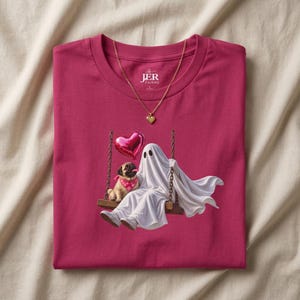 May include: A magenta crew neck t-shirt featuring a graphic of a white ghost and a pug wearing a pink bandana sitting on a swing with a red heart-shaped balloon. The shirt includes a gold heart pendant necklace and the text The JER Factory.