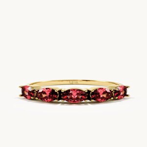 Peut inclure: Une bague en or ornée de cinq pierres précieuses rouges de taille ovale disposées en ligne. L'anneau en métal présente une finition polie et les pierres sont fixées par de petites griffes. La bague est présentée horizontalement sur un fond clair.