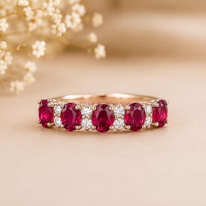 Op de afbeelding: Een ring van roségoud met vier ovaal geslepen dieprode robijnen, afgewisseld met paren kleine, rond geslepen witte diamanten. De ringband is van gepolijst roségoud en de stenen zijn in een horizontale rij bovenop de ring gezet.