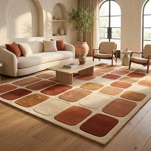 Puede incluir: Una alfombra rectangular grande con un patrón de cuadrícula repetitivo de rectángulos redondeados en tonos terracota, naranja quemado, crema y beige. La alfombra tiene un pelo suave y texturizado y cubre gran parte del suelo de madera.