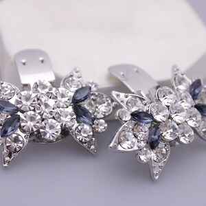 Puede incluir: Un par de pinzas para el pelo plateadas con un dise&ntilde;o floral. Cada pinza est&aacute; adornada con diamantes de imitaci&oacute;n transparentes y azul oscuro.