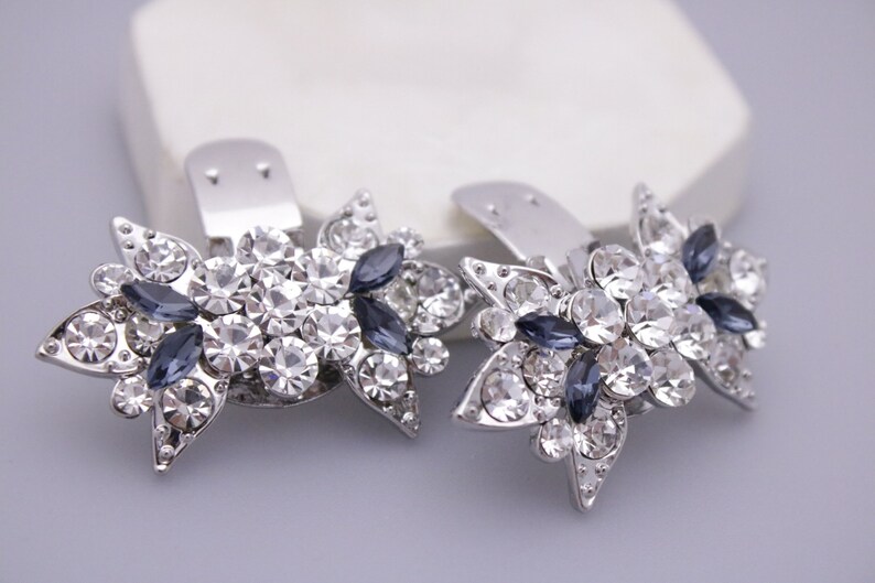 Puede incluir: Un par de pinzas para el pelo plateadas con un dise&ntilde;o floral. Cada pinza est&aacute; adornada con diamantes de imitaci&oacute;n transparentes y azul oscuro.