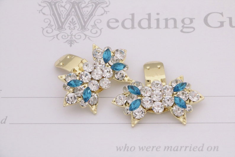Puede incluir: Dos pinzas para el pelo doradas con un dise&ntilde;o de estrella. Cada pinza est&aacute; adornada con diamantes de imitaci&oacute;n transparentes y azules.
