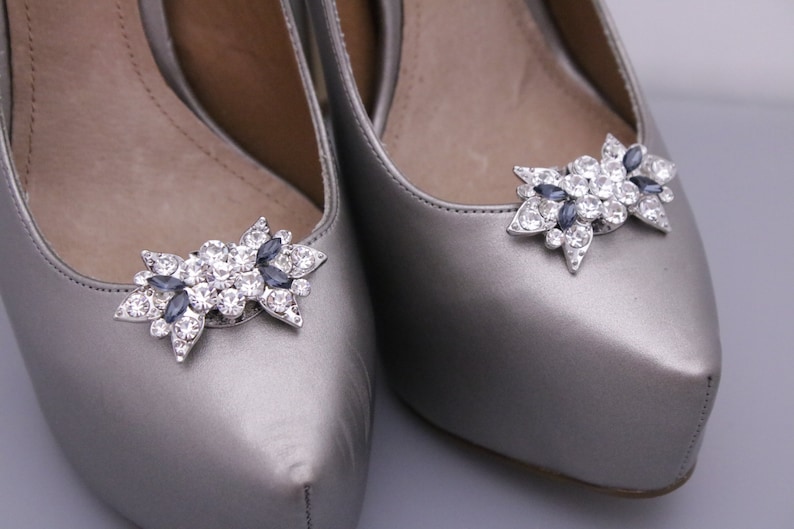 Puede incluir: Un par de zapatos plateados con un par de clips para zapatos de pedrer&iacute;a plateados y azules.