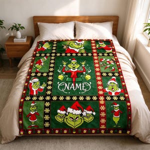 May include: A green fleece blanket featuring a grid pattern with multiple illustrations of a green character wearing a red Santa hat and coat. The center panel displays the character emerging from a gift box with the word NAME printed below.