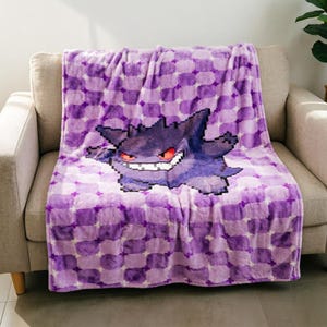 以下が含まれることがあります： ポケモンシリーズのピクセル化された紫色のゲンガーが描かれたプラッシュブランケット。ブランケットには紫と白の様々な色合いの市松模様が繰り返されており、中央には濃い紫色のゲンガーのグラフィックが配置されています。