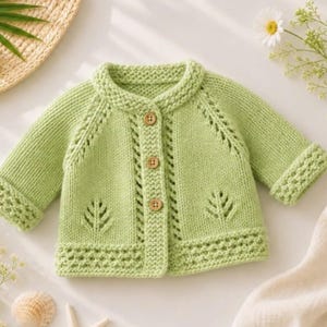 May include: A light green knitted cardigan featuring long sleeves with cuffed hems, a round neckline, and three wooden buttons down the centre. The garment displays a textured knit pattern with vertical eyelet details and leaf-shaped cutouts.