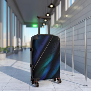 May include: A rolling suitcase featuring a dark, abstract pattern of diagonal lines in shades of deep blue, purple, and teal. The luggage has a black telescopic handle, four double-spinner wheels, and reinforced corner protectors on the top edges.