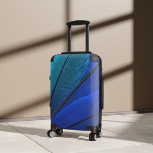Puede incluir: Una maleta rígida vertical con un vibrante patrón degradado que transita de turquesa a azul profundo. El exterior muestra un diseño texturizado de líneas diagonales negras, complementado con un asa telescópica negra y cuatro ruedas.