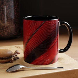 May include: A ceramic mug featuring a vibrant red and black diagonal striped pattern with a glossy finish. The mug has a solid black interior and a matching black handle. The design consists of thin, precise lines creating a dynamic visual effect.