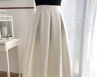 May include: A white pleated midi skirt with a high waist. The skirt is made of a smooth, satin-like fabric.