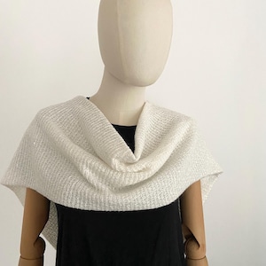 May include: A white knitted cowl neck scarf with a loose, drapey fit. The scarf is made of a soft, lightweight material and has a subtle texture.