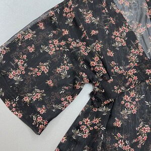 May include: A black sheer top with a floral print and a V-neckline. The top has a tie at the waist and 3/4 sleeves. The label reads "Thread & Grace".