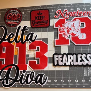 May include: A collection of embroidered patches including a circular patch with the text I CAN DO ALL THINGS THROUGH GOD, a square patch with KEEP GROWING, a large red and white elephant patch with the number 13, and Delta 1913 Diva text.