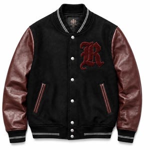 Op de afbeelding: Een zwart varsity-jack met donkerbordeauxrode leren mouwen, voorzien van een grote geborduurde bordeauxrode letter R op de linkerborst. Het jack heeft een drukknoopsluiting, twee zijzakken met bordeauxrode biezen en gestreepte geribbelde boorden.