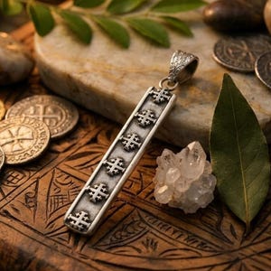 May include: A rectangular silver pendant featuring a series of six embossed Jerusalem crosses arranged vertically along its length. The pendant has a textured, oxidized finish and includes a decorative, engraved bail at the top for attachment.