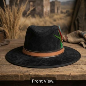 Puede incluir: Un sombrero fedora negro con ala ancha y copa pellizcada. El sombrero presenta una banda de cuero color canela alrededor de la base y un acento decorativo de plumas verdes, rojas y negras en el lateral. La superficie tiene una textura mate suave.