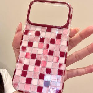 May include: A protective phone case featuring a grid pattern of small square tiles in varying shades of deep burgundy, bright pink, and soft white. The case has a clear, glossy finish and a solid dark burgundy border around the camera cutout area.