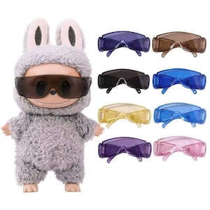 May include: A plush doll with grey fur and rabbit ears wearing dark brown goggles, accompanied by eight additional pairs of goggles in various translucent colours including blue, purple, yellow, pink, brown, and black, arranged in two vertical columns.