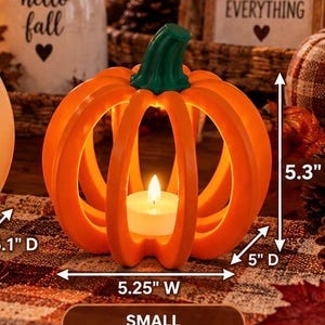 May include: An orange pumpkin-shaped candle holder with a green stem, featuring a hollow slatted design and a white tea light candle inside. The dimensions are clearly labeled as 5.25 inches wide, 5 inches deep, and 5.3 inches high.
