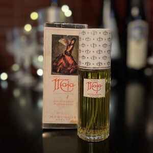 May include: A vintage bottle of "Nueva Maja" cologne by Myrurgia, Spain. The bottle is clear glass with a gold-colored cap and a white label with gold lettering. The box is red, white, and gold with a picture of a woman in a red dress.