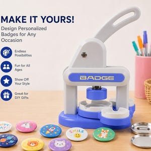 Könnte beinhalten: Eine blau-graue Buttonmaschine mit Hebel, die den Text "MAKE IT YOURS!" und "BADGE" auf dem Rahmen trägt. Mehrere bunte, runde Ansteckbuttons mit verschiedenen grafischen Motiven sind vor der Maschine angeordnet.