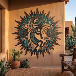 May include: A circular wall art piece featuring a stylized Kokopelli figure playing a flute, surrounded by sun rays, cacti, and floral patterns in shades of turquoise, brown, and tan, mounted on a smooth, light-colored exterior wall surface.