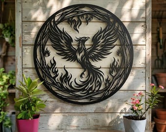 May include: A circular black metal wall art piece featuring a laser-cut design of a phoenix rising from flames. The mythical bird is depicted with wings spread wide, surrounded by stylized fire patterns within a thin circular frame border.
