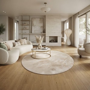 May include: A living room featuring a curved cream-coloured sofa with textured fabric, a round coffee table with a white top and gold frame, and a large circular beige area rug. The space includes a fireplace, wooden flooring, and neutral decor.