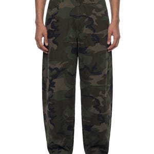 Puede incluir: Pantalones largos con un patrón de camuflaje boscoso clásico en tonos verde oscuro, oliva, marrón y negro. Estos pantalones tienen una cintura estructurada con cierre de un solo botón, trabillas para cinturón y un corte recto y relajado.