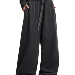 Könnte beinhalten: Dunkelgraue Jogginghose mit weitem Bein, elastischem Bund mit passendem Kordelzug und Seitentaschen. Der Stoff hat eine leicht verwaschene Optik und die Hose reicht bis zum Boden.