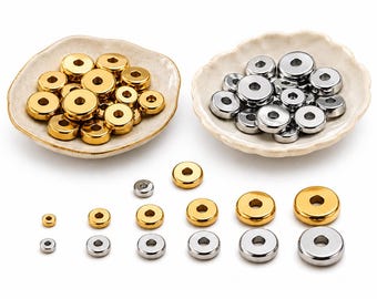 Könnte beinhalten: Eine Sammlung runder, flacher Metallperlen mit einem Mittelloch in Gold- und Silbertönen. Die Perlen sind in zwei kleinen Schalen mit gewelltem Rand sowie in einer nach Größe sortierten Reihe angeordnet und zeigen verschiedene Durchmesser.